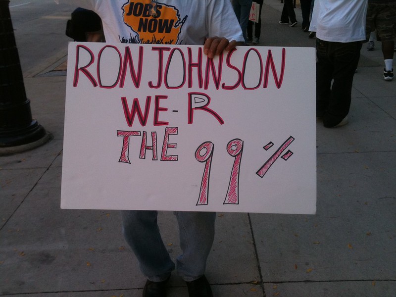 A protestor holds a sign reading "Ron Johnson R are the 99%"
