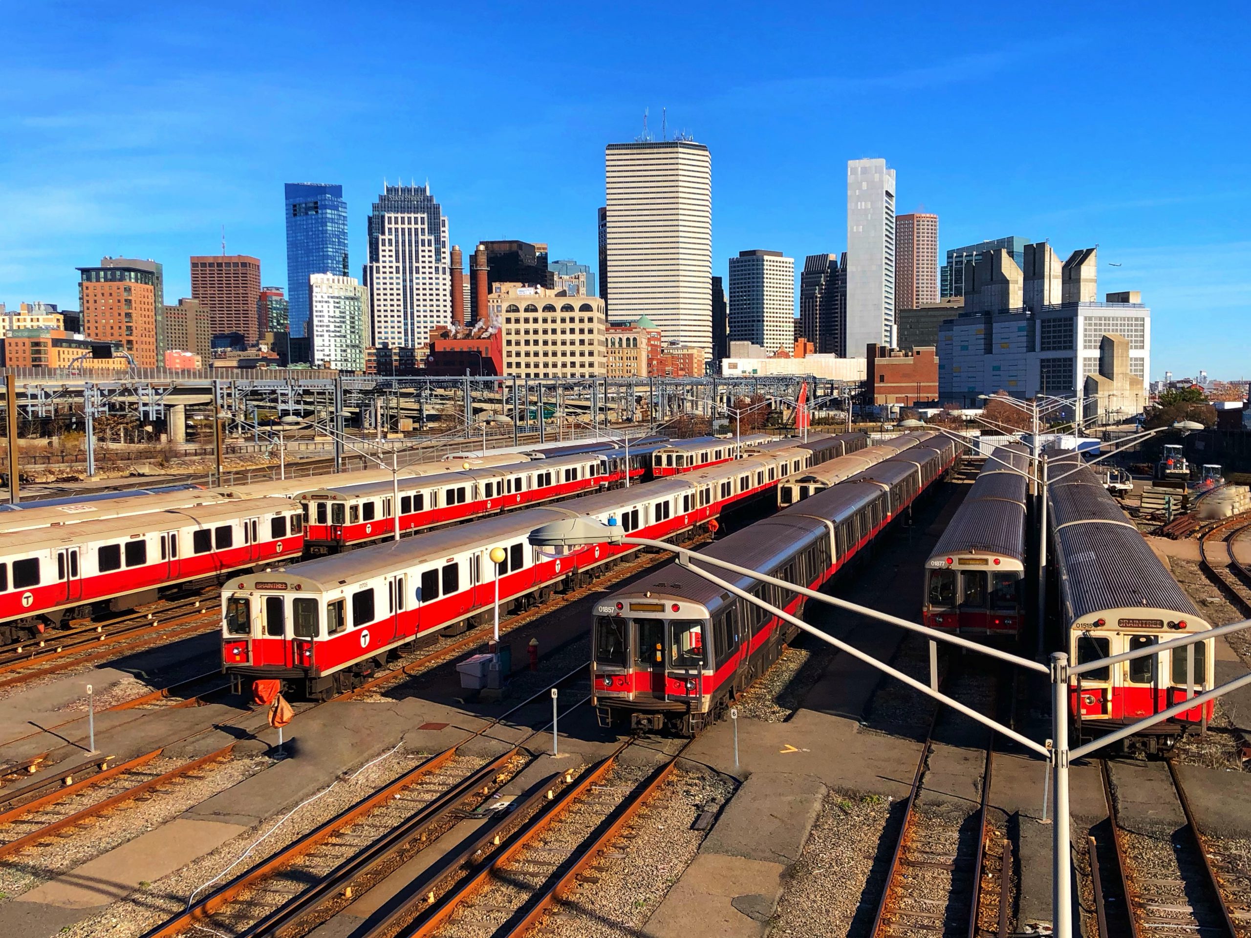 Several Red Line trains wait on the tracks with the Boston skyline in the background.